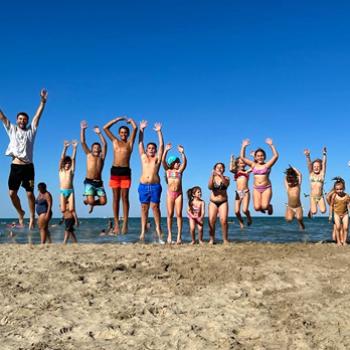 Gruppo di persone sorridenti in cerchio, indossano magliette blu con una lettera gialla.